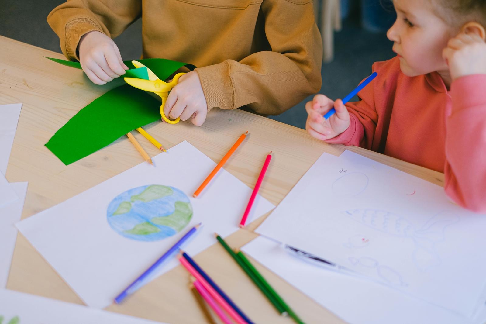 Two young children crafting using paper, coloured pencils and scissors