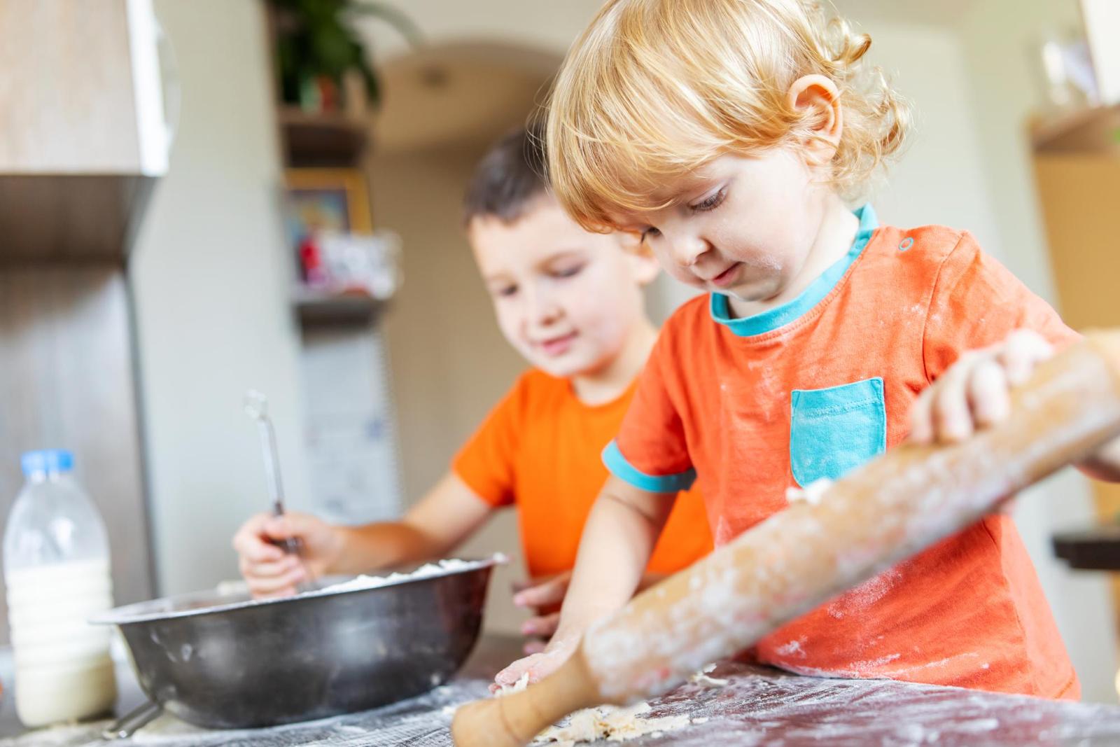 2 young boys aged 3 and 5 baking. Older boy mixing and younger boy rolling out pastry.