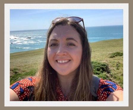 A selfie of a woman with brown hair with grass and sea in the background.